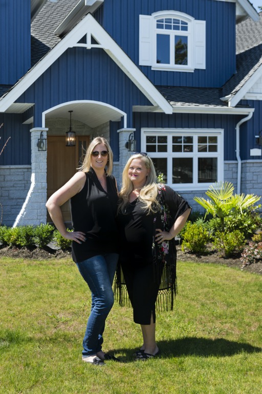 Sarah and a happy client stand outside a beautiful blue house with white trim and grey stone.