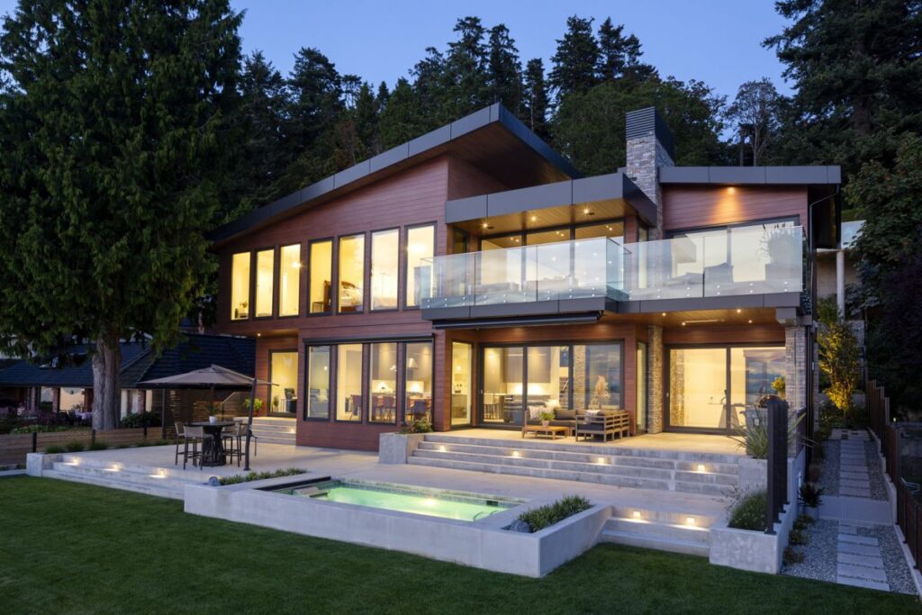 Beyond the swimming pool sits a beautiful home with many windows lit by warm yellow light.