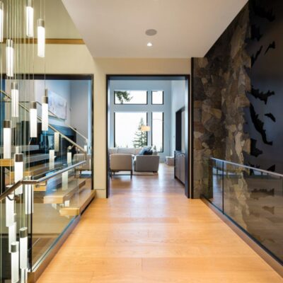 View into a spacious entryway with a striking side staircase featuring a cascading pendant light, stone accent wall, and a glimpse of the living room beyond, highlighting the home's grand vertical design.