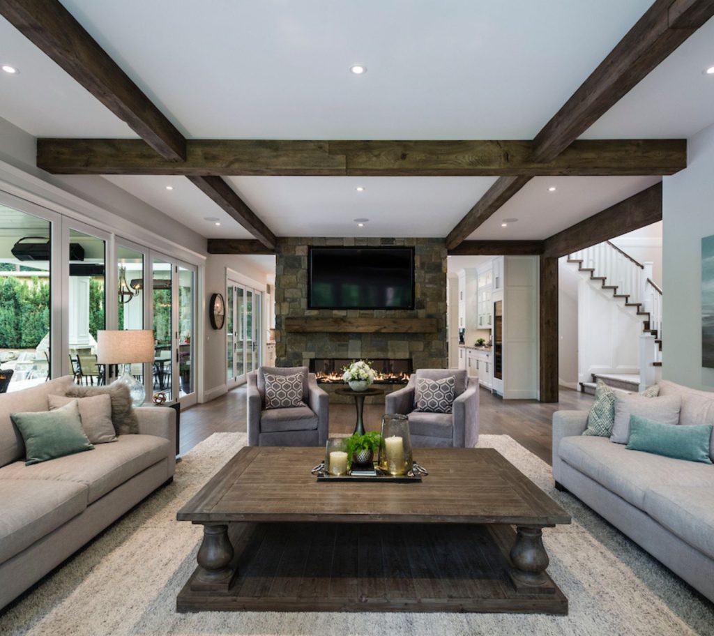 A gorgeous living room with oversized wood square coffee table, two grey couches on either side, and two grey armchairs at the far end of the table. 