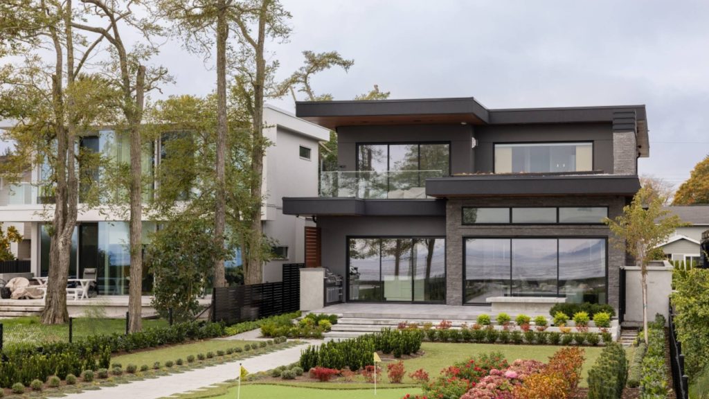 Modern West Coast contemporary custom home with clean rooflines, large black-framed windows, layered landscaping, and ocean views in British Columbia.