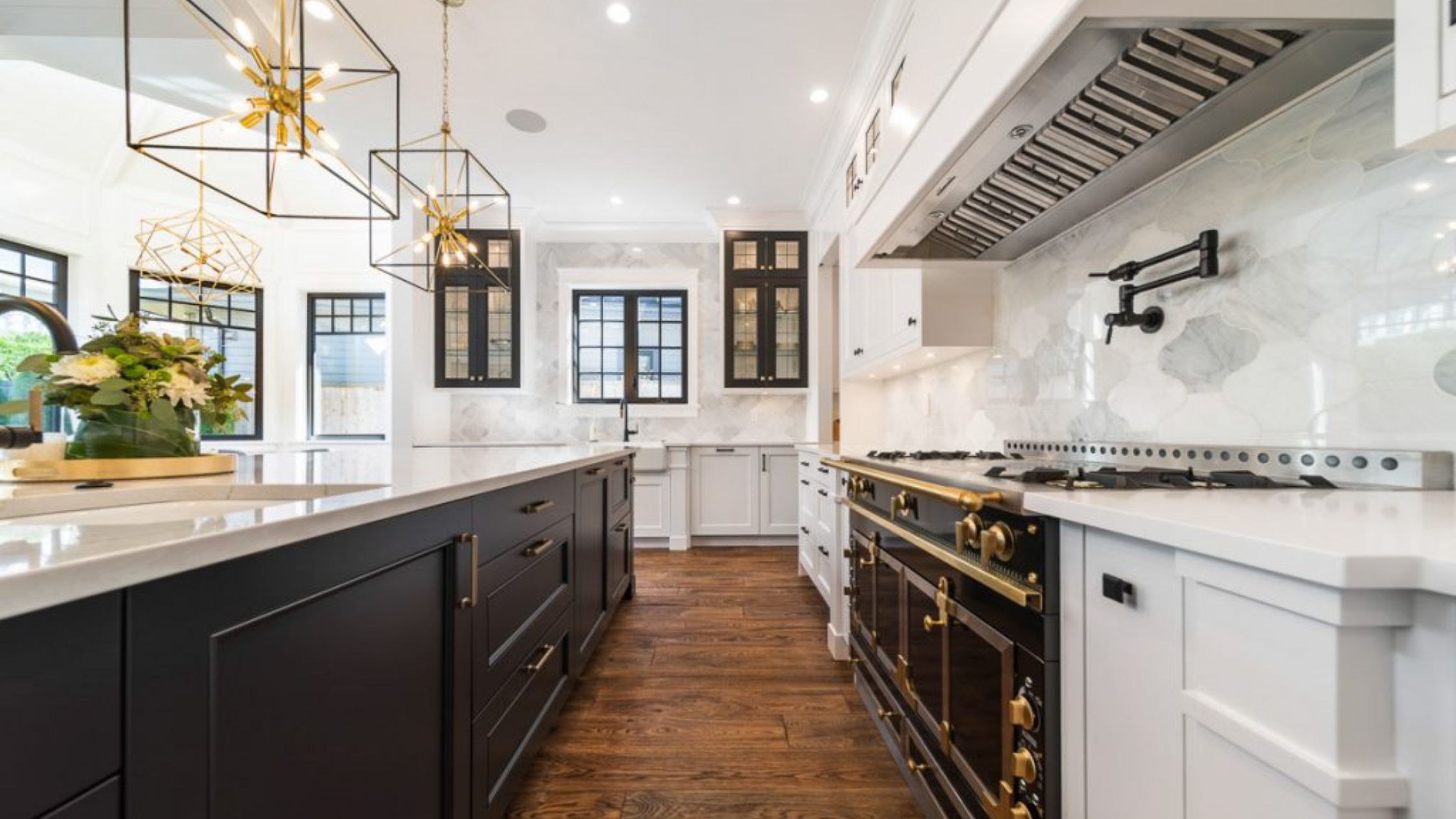 Luxury black and white kitchen design with large island, custom cabinetry, marble backsplash, brass hardware, and statement pendant lighting.